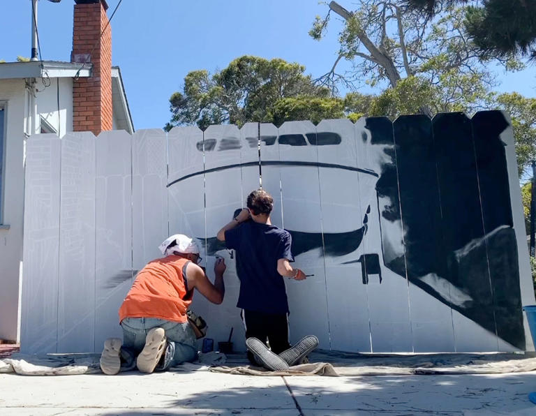 Artists paint a hyper-realistic mural on a fence in the home driveway of Etienne Constable in Seaside, California.