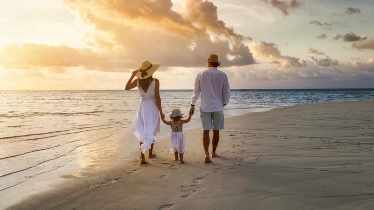 A family walks hand in hand down a tropical paradise beach during sunset