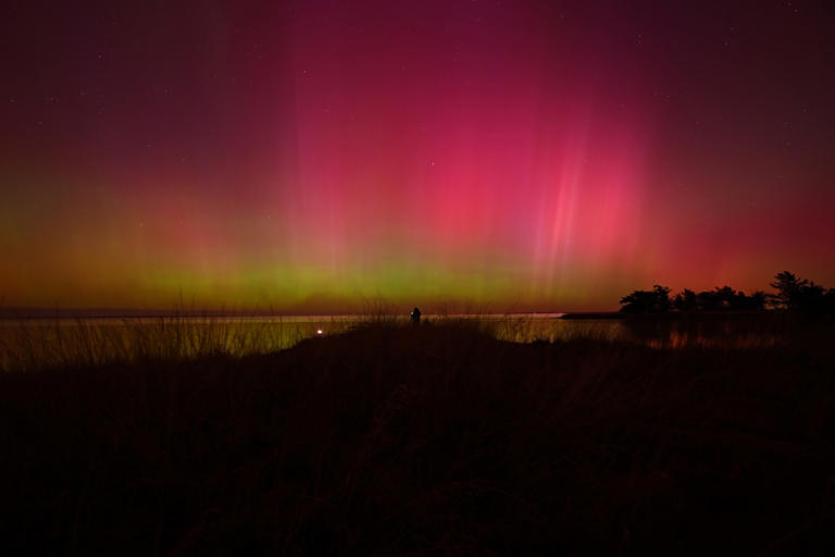 A photographer takes pictures of the Aurora Australis, also known as the Southern Lights, glow on the horizon over waters of Lake Ellesmere on the outskirts of Christchurch, New Zealand, on May 11, 2024