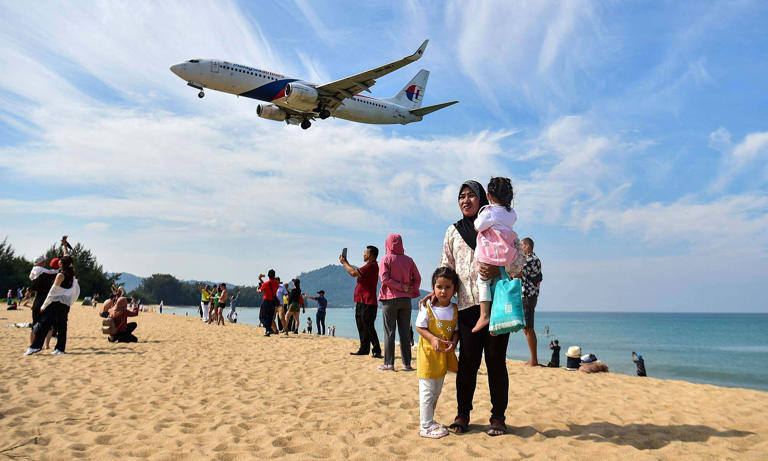 Tourists stand on Mai Khao Beach as a plane lands at Phuket International Airport in Thailand, 2023. Photo by AFP
