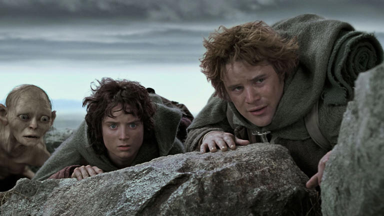 image from the 2002 movie "The Lord of the Rings: The Two Towers." Pictured, from left to right, are characters Gollum, Frodo and Sam, who are all crouching down behind rocks with just their heads showing as they are looking intently at something.