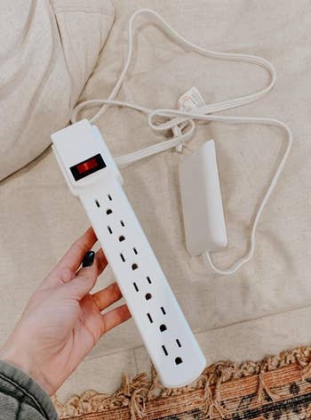 a reviewer photo of a hand holding the outlet cover with a power strip attached