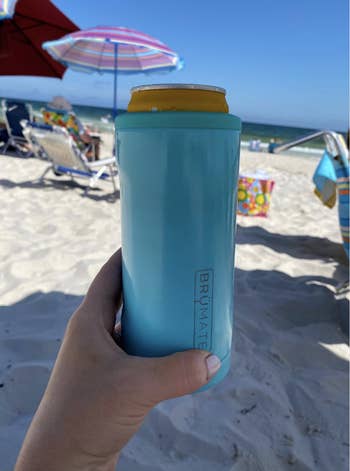 Reviewer holding up a blue insulated can cooler at the beach
