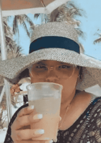 a reviewer wearing the hat and drinking a cocktail
