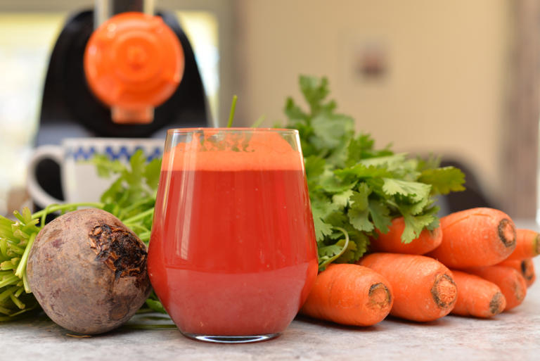 Carrot and Beetroot juice freshly extracted showing juicer in the background along with Carrots and Beetroot, shot in landscape mode with a mixture of natural and artificial light