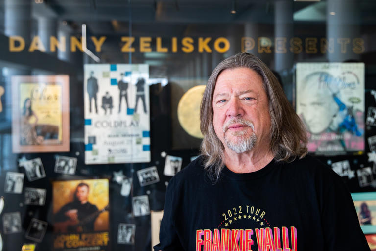 Danny Zelisko poses for a portrait in front of the new museum exhibit on the fourth level of Terminal 3 at Phoenix Sky Harbor International Airport on May 10, 2023. The exhibit showcases several items from Danny Zelisko's personal collection of signed photographs, concert posters and guitars.