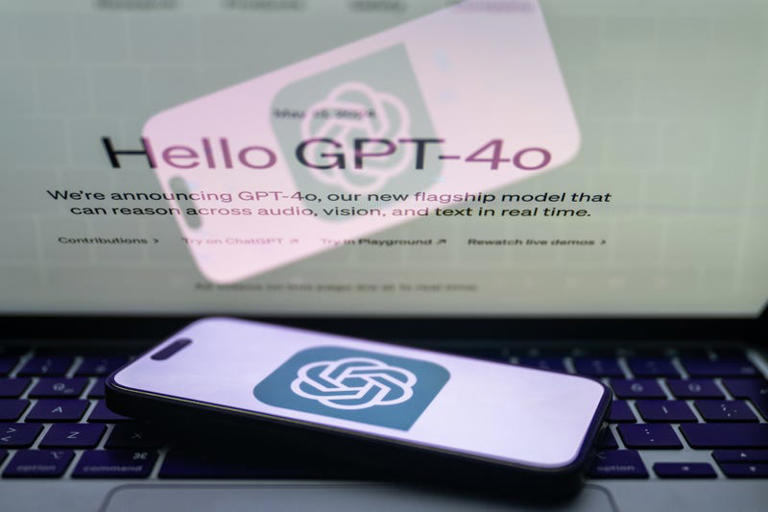 'Chat GPT' logo is displayed on a mobile phone screen in front of a computer screen