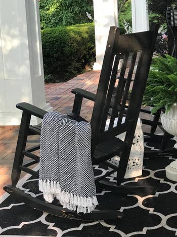 a reviewer photo of a rocking chair on a porch with the blanket in black draped over it
