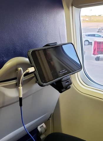 A phone mounted to the back of an airplane tray table using a black clip device