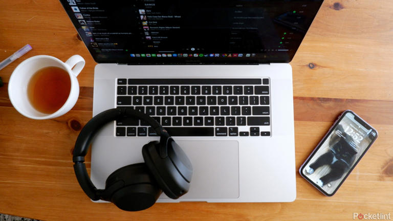 The Sony WH-1000XM4 resting on a laptop on a coffee table, next to a phone and a cup of tea.