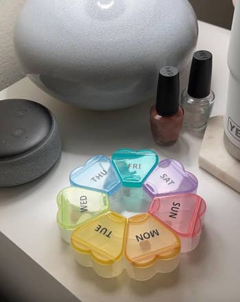 A round rainbow themed pill box with the days in the shape of hearts that form a flower
