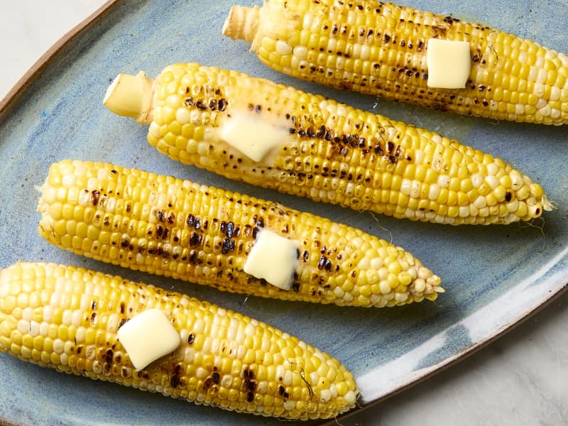 overhead shot of four ears of grilled corn on a blue platter