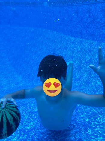 Child underwater holding a ball, smiling with eyes closed