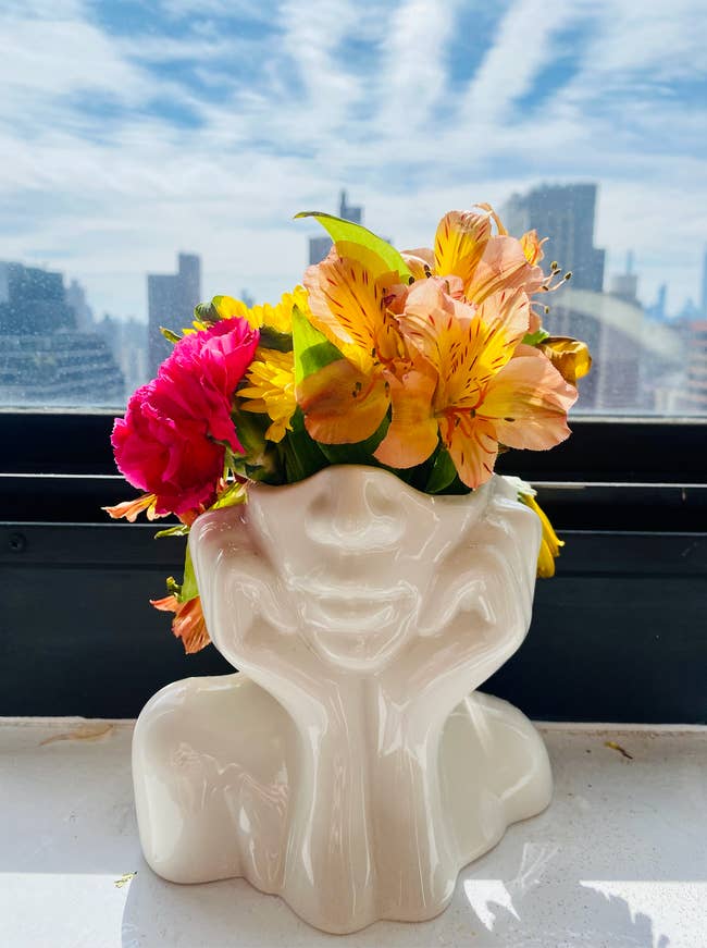 A white vase depicting the bottom half of a face with its head in its hands