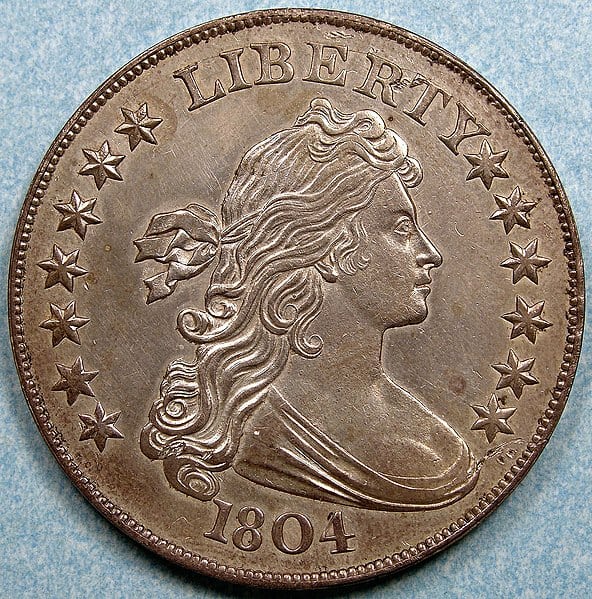 <p><span>Known as the “King of American Coins,” the 1804 Silver Dollar is highly prized by collectors due to its storied history and extreme rarity. Only 15 specimens are known to exist, produced in three different classes. This coin was minted for diplomatic gifts, making it even more unique. The intricate design features Lady Liberty on one side and a heraldic eagle on the reverse, showcasing the detailed craftsmanship of the era.</span></p>