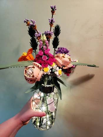 a hand holding a vase with the lego flowers inside, plus fairy lights
