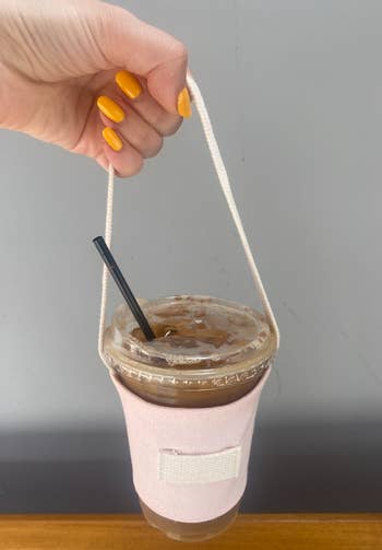 editor holding an iced coffee in a sleeve with a long handle by the hand