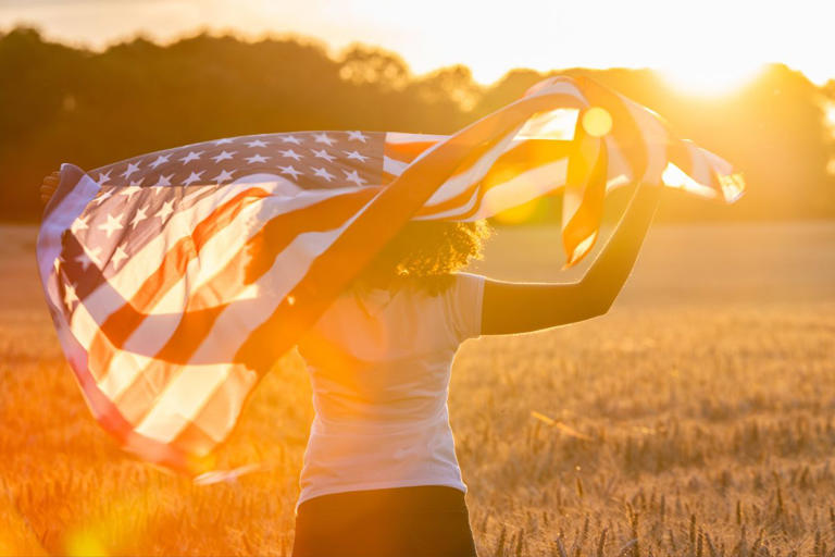 girl holding American flag in a field with sunlight shining on her
