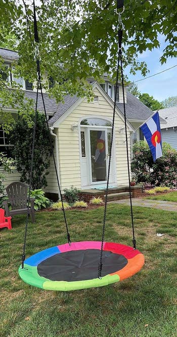 Circular tree swing hanging in a backyard with a house in the background