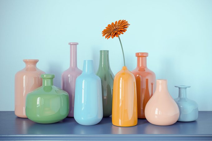 Multicolored Bottles Vases from Glass with one Daisy Flower on Blue Dresser and Blue Wall Abstract Background. 3D Rendering. Vintage Retro Colored