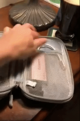 Reviewer opening a gray zippered cord organizer to show the two different compartments holding electronics