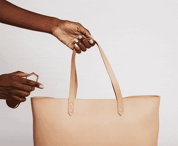 a gif of a model attaching the luggage tag to a tote and clipping a wide--brim hat to the luggage tag