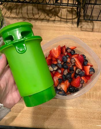 Reviewer holding green cylinder shaped cutter next to a tupperware of cut fruit