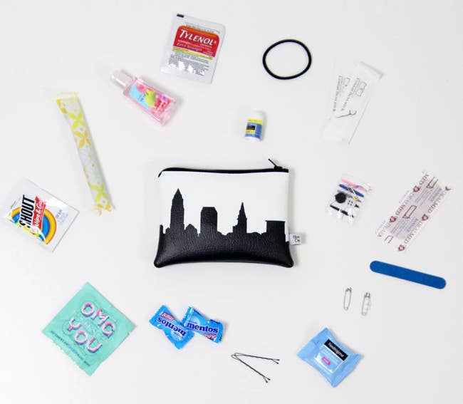 A small white faux leather pouch with a black skyline print surrounded by a mix of travel-sized toiletries and on-the-go essentials