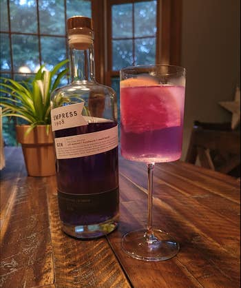 A cylinder shaped stemmed clear wine glass with pink gin in it
