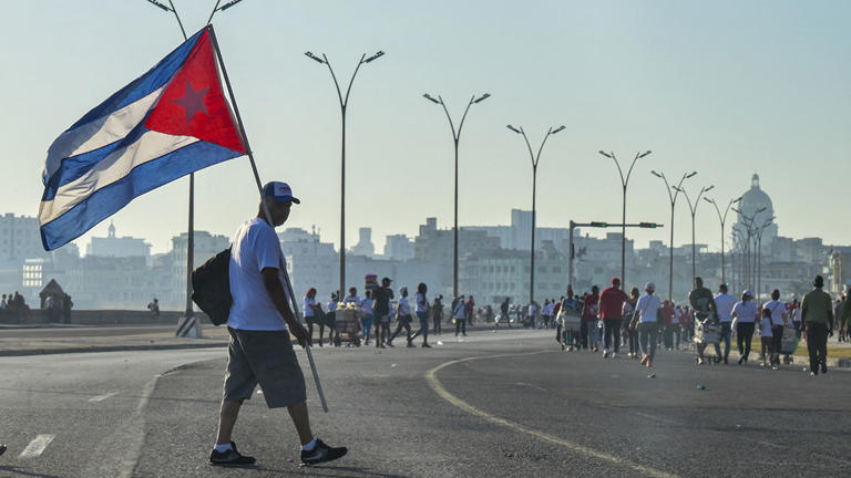Foreign tourists hold flags of Euskadi (L) and Cuba as they walk at Havana’s waterfront after participating in the commemoration of May Day (Labour Day) to mark the international day of the workers at the Anti-imperialist Tribune in front of the US Embassy in Havana on May 1, 2024. (Photo by ADALBERTO ROQUE / AFP) (Photo by ADALBERTO ROQUE/AFP via Getty Images)
