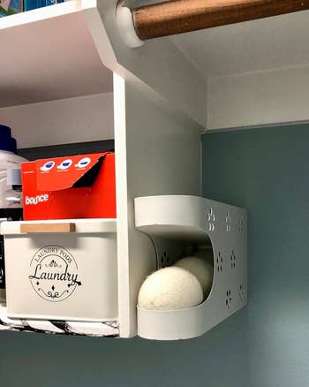 A wall-mounted laundry dispenser with wool dryer balls and a box of fabric softener sheets on a shelf above
