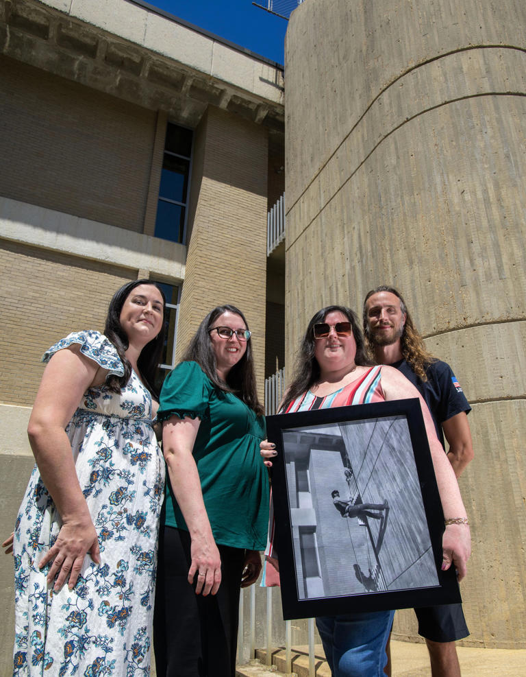 Samantha Wacob, Jessica Marsh, Rebecca Marsh and Jake Marsh, children UWF physics professor Dr. James Marsh, show a photo of their dad rappelling down the side of the UWF Physics building. To honor their father, they have put his remains aboard a Celestis Voyager spacecraft that will orbit the sun for eternity.