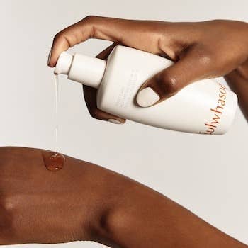 Close-up of a person dispensing skincare lotion onto their hand from a white bottle