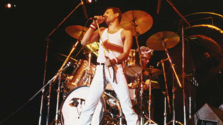 Freddie Mercury (1946-1991), singer with Queen, standing in front of a drumkit as he sings into a microphone on stage during a live concert performance by the band at the National Bowl in Milton Keynes, England, United Kingdom, on 5 June 1982