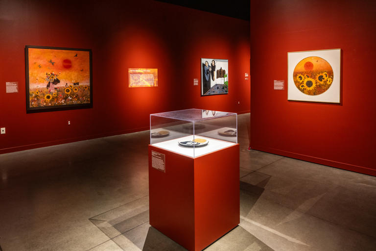 A museum exhibition of paintings and artifacts in a space with red walls
