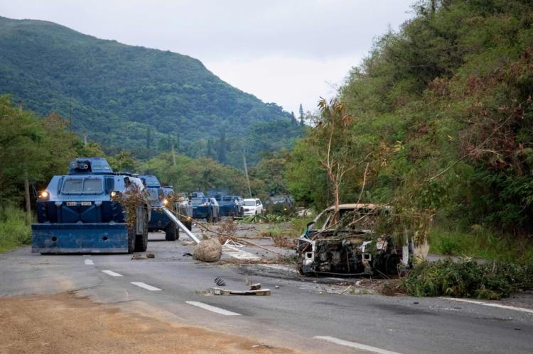 Un convoi de véhicules blindés de la gendarmerie française débarrasse la chaussée des voitures incendiées et autres branches et débris utilisés par les indépendantistes, pour filtrer la circulation au col de La Pirogue, dans la commune de Paita, territoire français du Pacifique de Nouvelle-Calédonie, le 19 mai 2024.