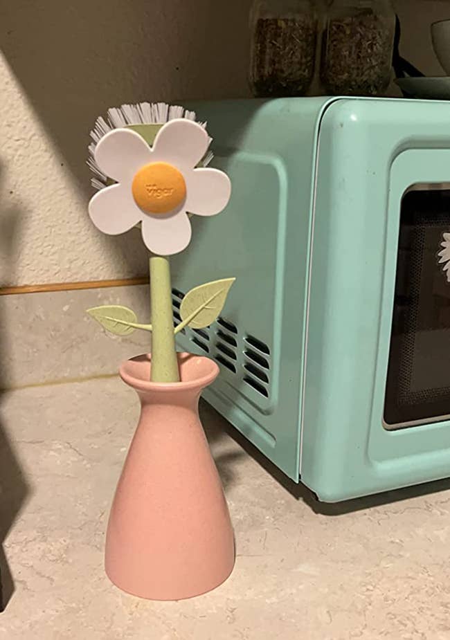 a white daisy shaped scrubber with its stem in a pink vase