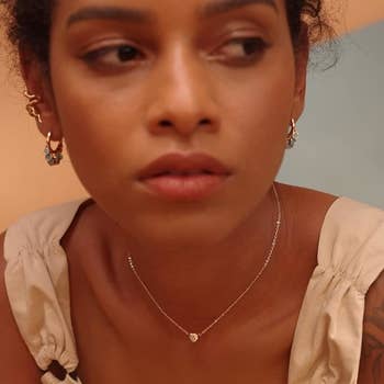 a model wearing a thin chain with a gold heart on it with an 'a' inside