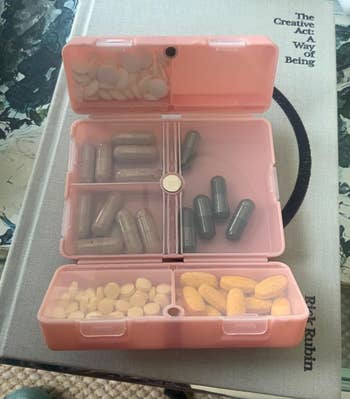 A pink folding organizer open to show capsules inside of the clear-paneled compartments