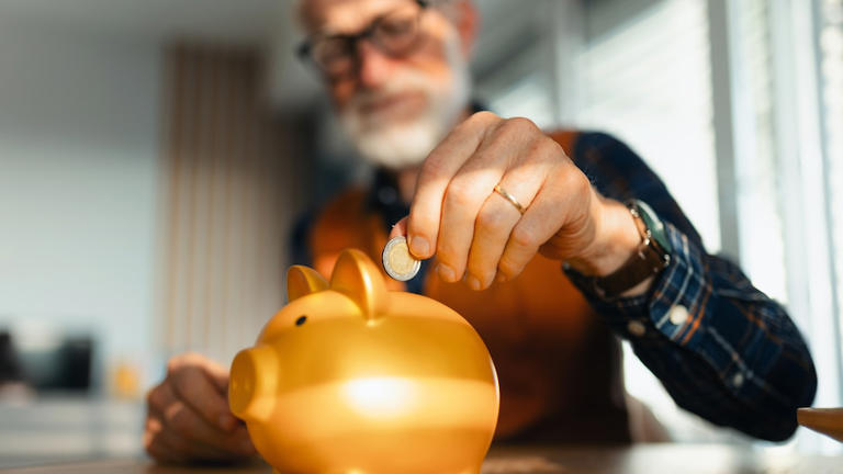 Ein älterer Mann wirft eine Euro-Münze in ein Sparschwein.