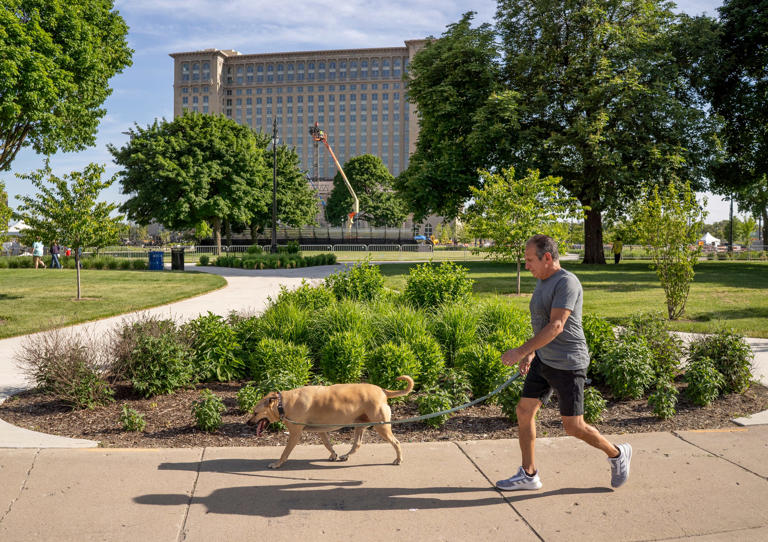 Ray Moncivais, of Detroit, walks his daughter's dog Kenda Joe through Roosevelt Park near his Corktown neighborhood after work on Friday, May 31, 2024. Moncivais has lived in Corktown since childhood and witnessed the changing landscape of the neighborhood throughout its development. He does tile work around Detroit, and has previously done work on Cork and Gabel.