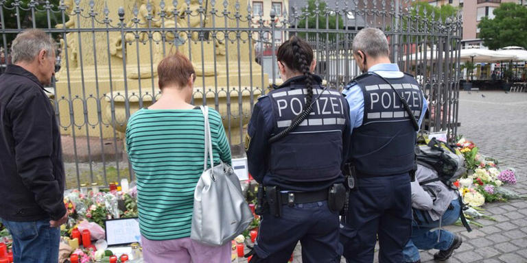 Zahlreiche Personen, darunter Polizisten, stehen in unmittelbarer Nähe des Tatorts vor niedergelegten Kerzen und Blumen. René Priebe/pr-video/dpa