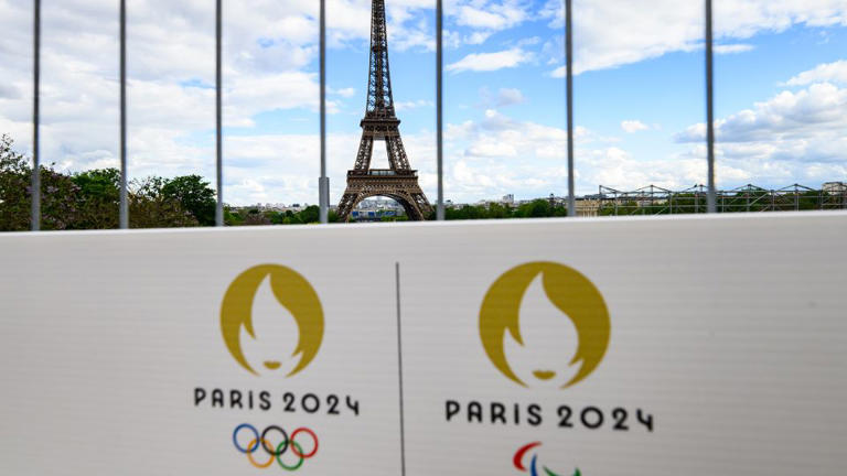 The Olympic rings and the Paralympic Games logo can be seen on a sign on a construction fence in front of the Eiffel Tower. The Olympic Games and Paralympics take place in France this summer.
