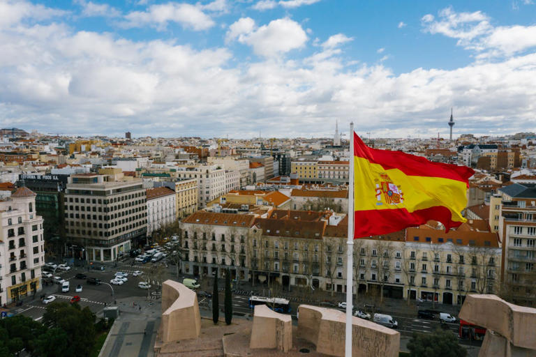 Madrid vs Barcelona. Pictured: Spanish national flag against cityscape.