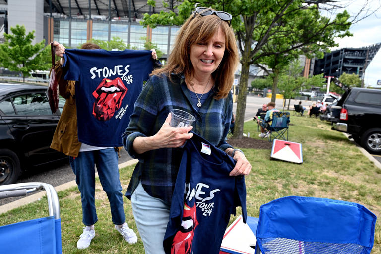 Beth Reinking (left) and Susan Gaunay (right) buy T-shirts from a passing vender as they tailgate with friends In the parking lot of the Wells Fargo Center Tuesday, June 11, 2024, ahead of the Rolling Stones impending performance at Lincoln Financial Field across the street. The women have been attend ending Stones concerts together since 1989. They where with a group who have been doing the same since the 70s.