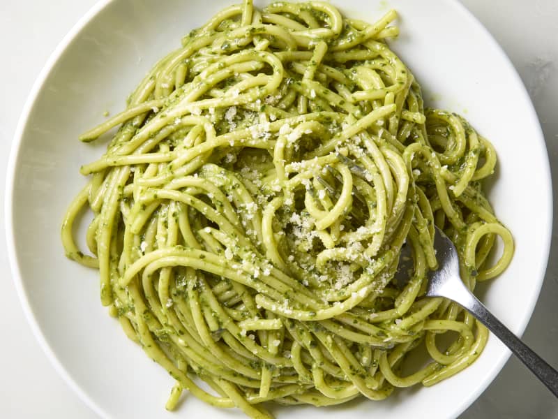 overhead shot of pesto pasta in a white bowl with a fork in it.