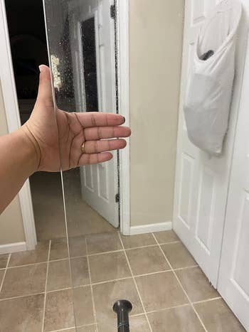 The same shower door with reviewer hand, but the door is completely clear and clean