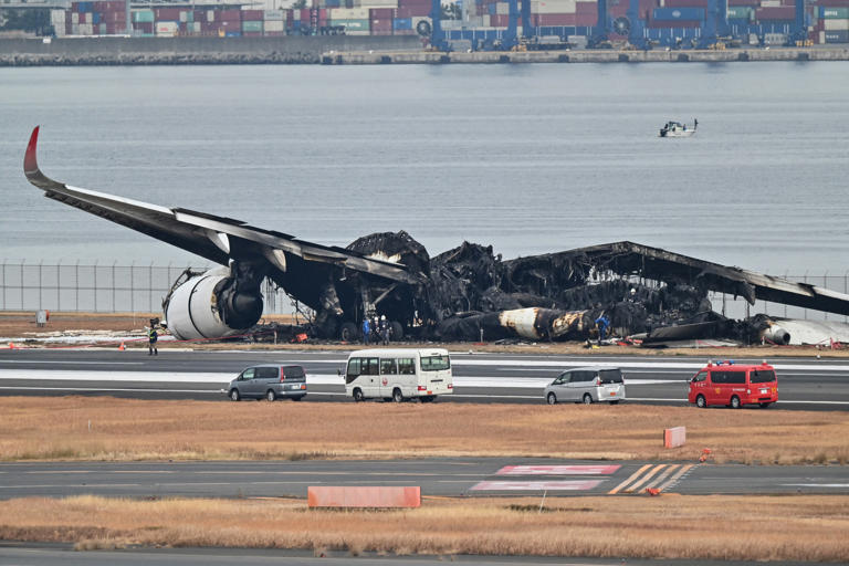 Officials look at the burnt wreckage of a Japan Airlines (JAL) passenger plane on the tarmac at Tokyo International Airport at Haneda in Tokyo on January 3, 2024, the morning after the JAL airliner hit a smaller coast guard plane on the ground.