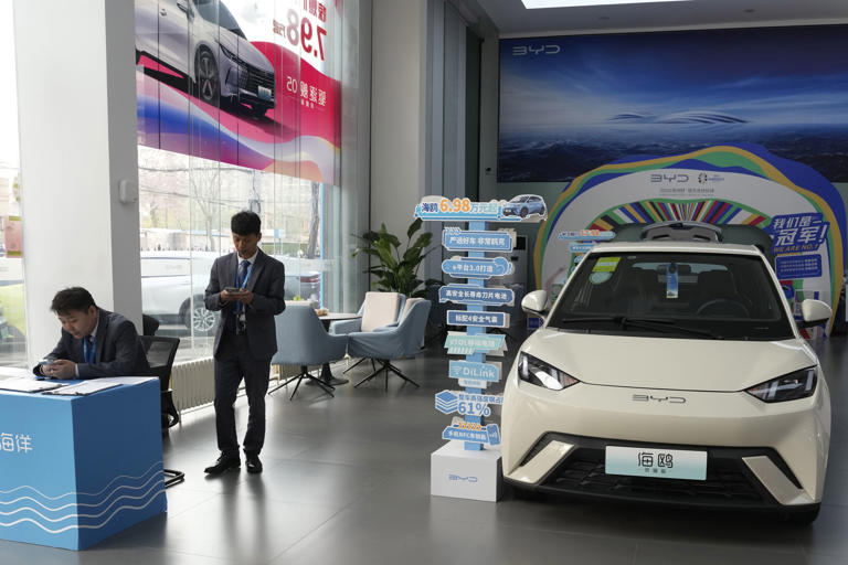 FILE - Sales staff stand near the Seagull electric vehicle from Chinese automaker BYD at a showroom in Beijing on April 10, 2024. Considered a marvel of engineering efficiency, its lightweight design allows the Seagull to go farther per charge on a smaller battery. (AP Photo/Ng Han Guan, File)