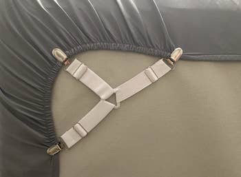 A white three way adjustable fastener hooked to a fitted sheet to pin it under a mattress